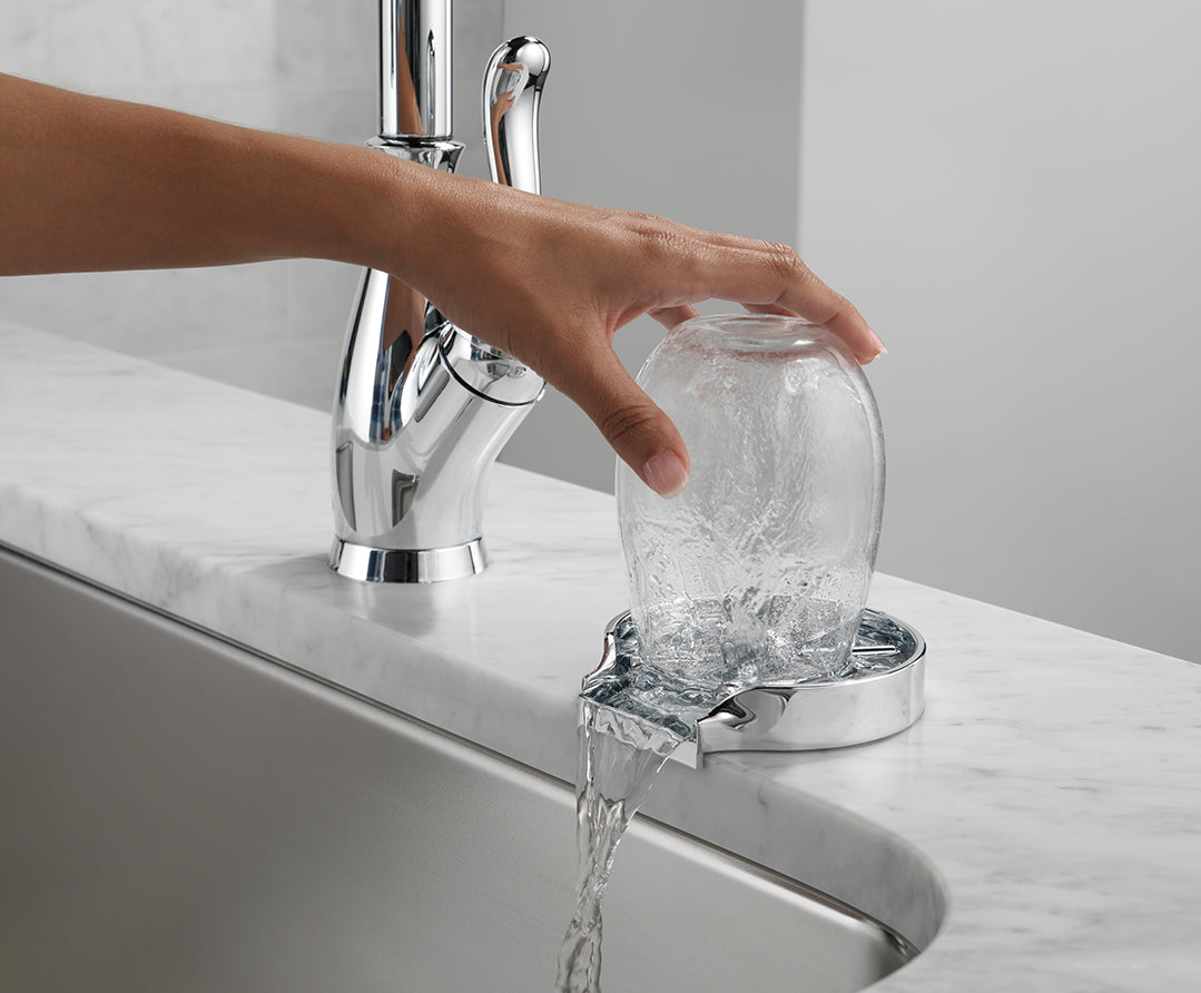 A hand using the glass rinser by rinsing a cup with the water flowing into the sink..